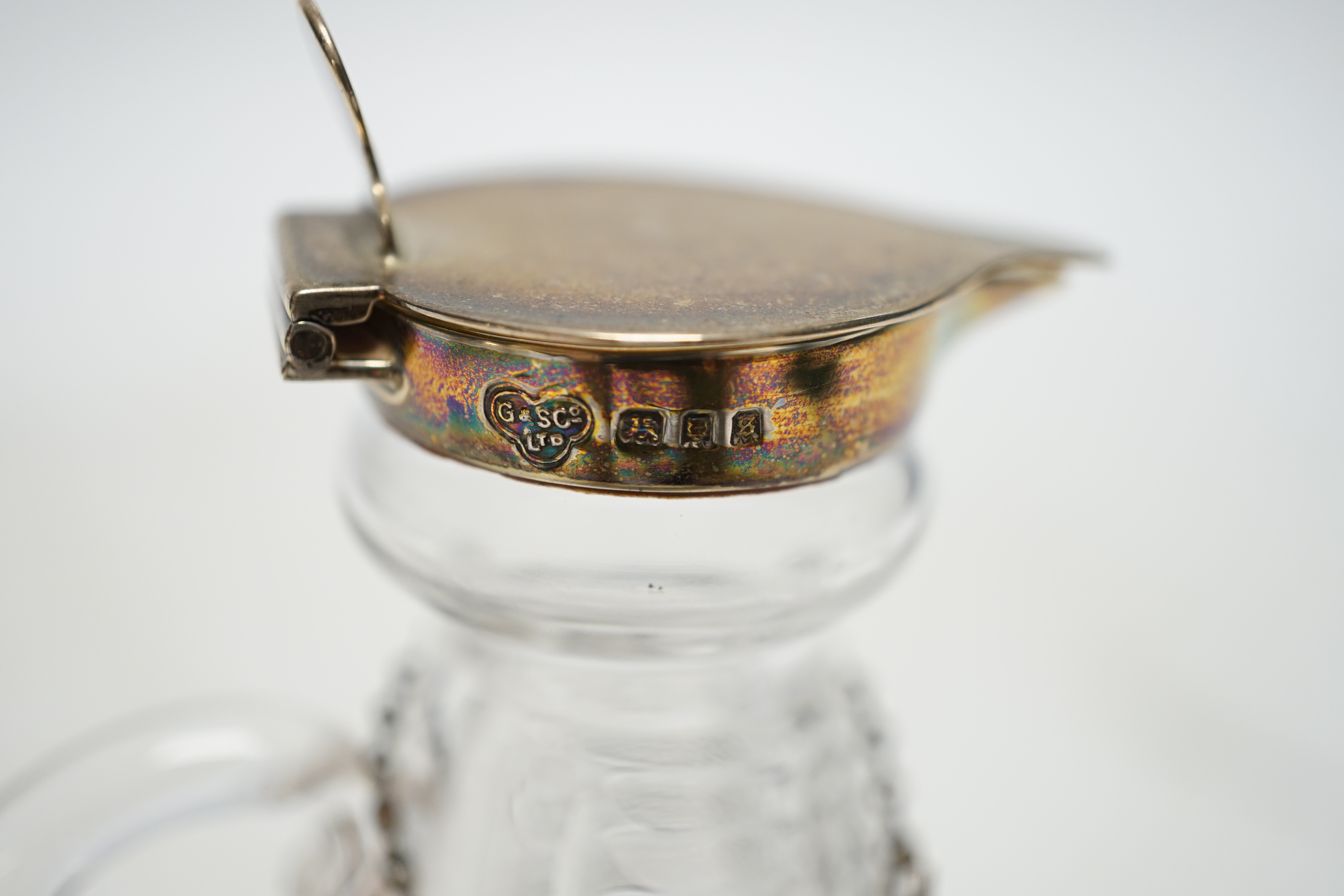 A George V silver mounted cut glass whisky noggin, Goldsmiths & Silversmiths Co Ltd, London, 1933, 10.9cm, with an Edwardian silver 'Whisky' wine label. Condition - poor
